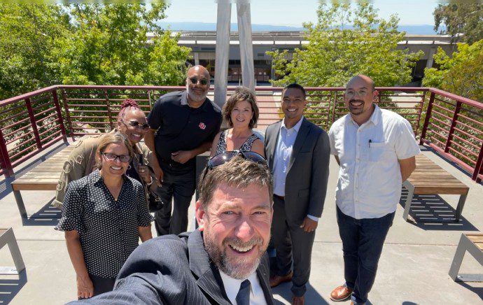 Group of seven people posing outdoors on a sunny day.