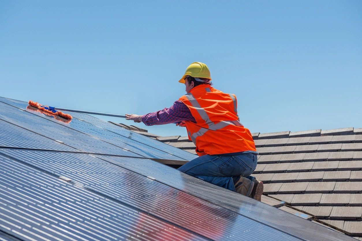 Worker installing solar panels on a rooftop under clear blue sky.